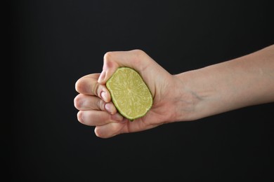Photo of Woman squeezing lime on black background, closeup