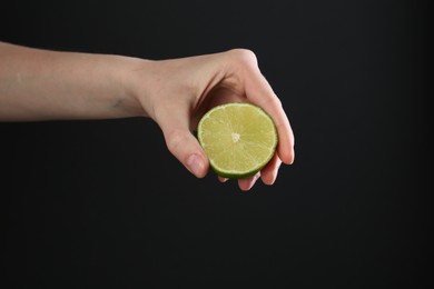 Photo of Woman squeezing lime on black background, closeup
