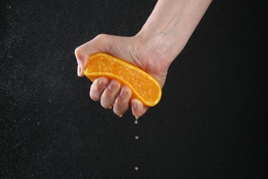 Photo of Woman squeezing orange on black background, closeup