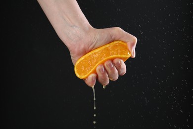 Photo of Woman squeezing orange on black background, closeup