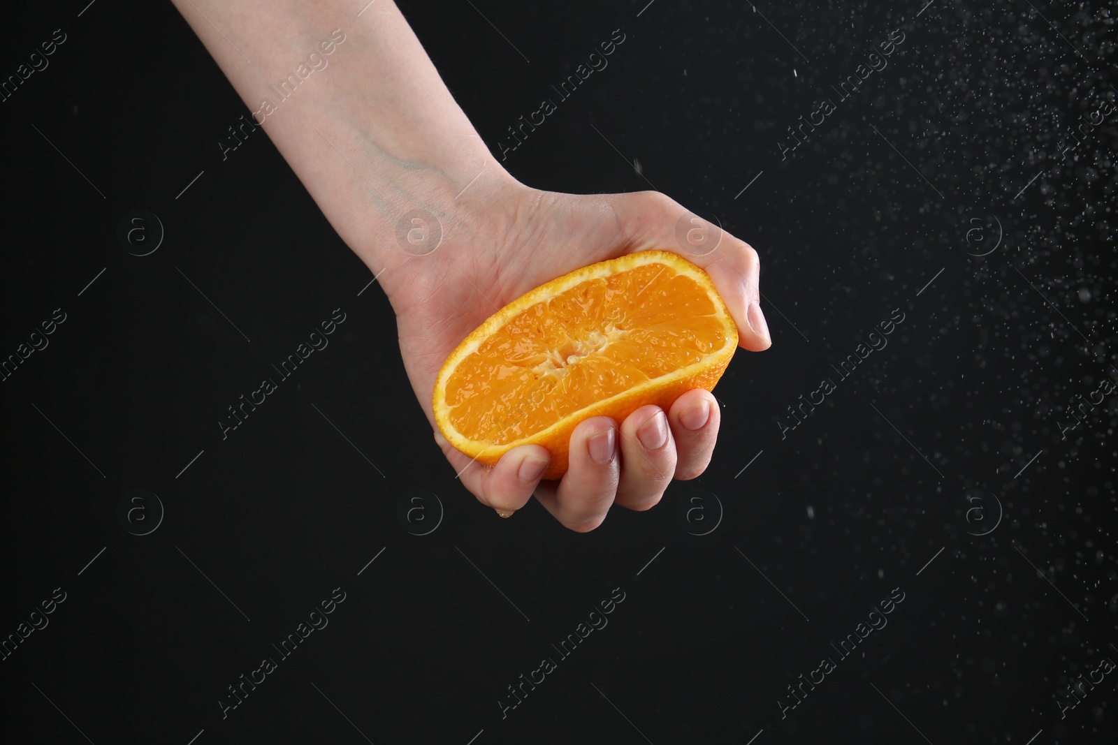 Woman squeezing orange on black background, closeup Photo of Woman squeezing orange on black background, closeup