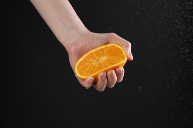 Photo of Woman squeezing orange on black background, closeup