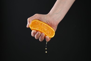 Photo of Woman squeezing orange on black background, closeup