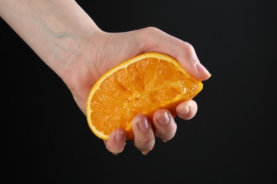 Photo of Woman squeezing orange on black background, closeup