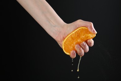 Photo of Woman squeezing orange on black background, closeup
