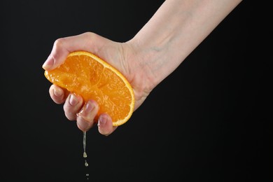 Photo of Woman squeezing orange on black background, closeup