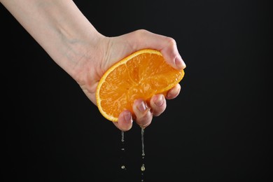 Photo of Woman squeezing orange on black background, closeup