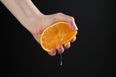 Photo of Woman squeezing orange on black background, closeup