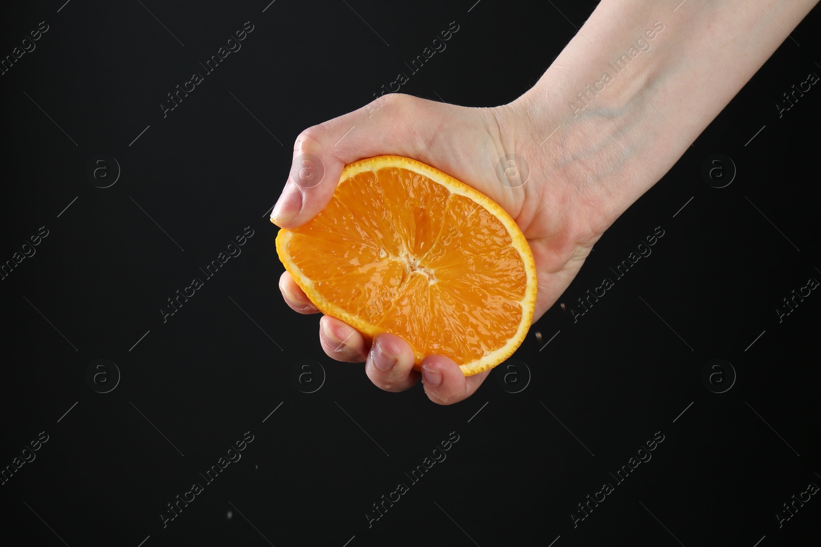 Woman squeezing orange on black background, closeup Photo of Woman squeezing orange on black background, closeup