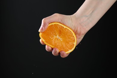 Photo of Woman squeezing orange on black background, closeup