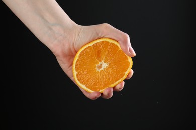 Photo of Woman squeezing orange on black background, closeup