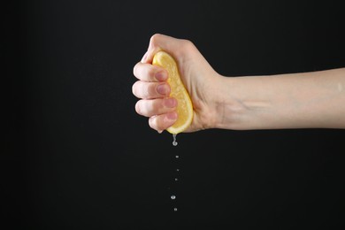 Photo of Woman squeezing lemon on black background, closeup. Space for text