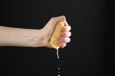 Photo of Woman squeezing lemon on black background, closeup. Space for text