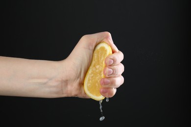 Photo of Woman squeezing lemon on black background, closeup