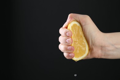 Photo of Woman squeezing lemon on black background, closeup. Space for text