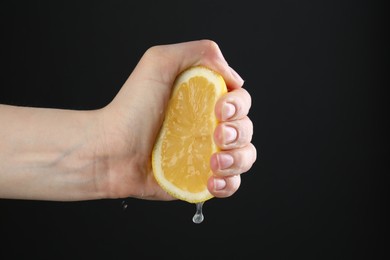 Photo of Woman squeezing lemon on black background, closeup