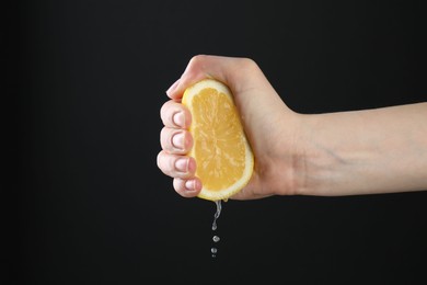 Photo of Woman squeezing lemon on black background, closeup