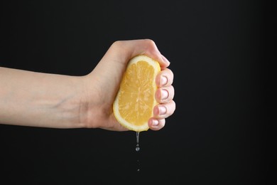 Photo of Woman squeezing lemon on black background, closeup