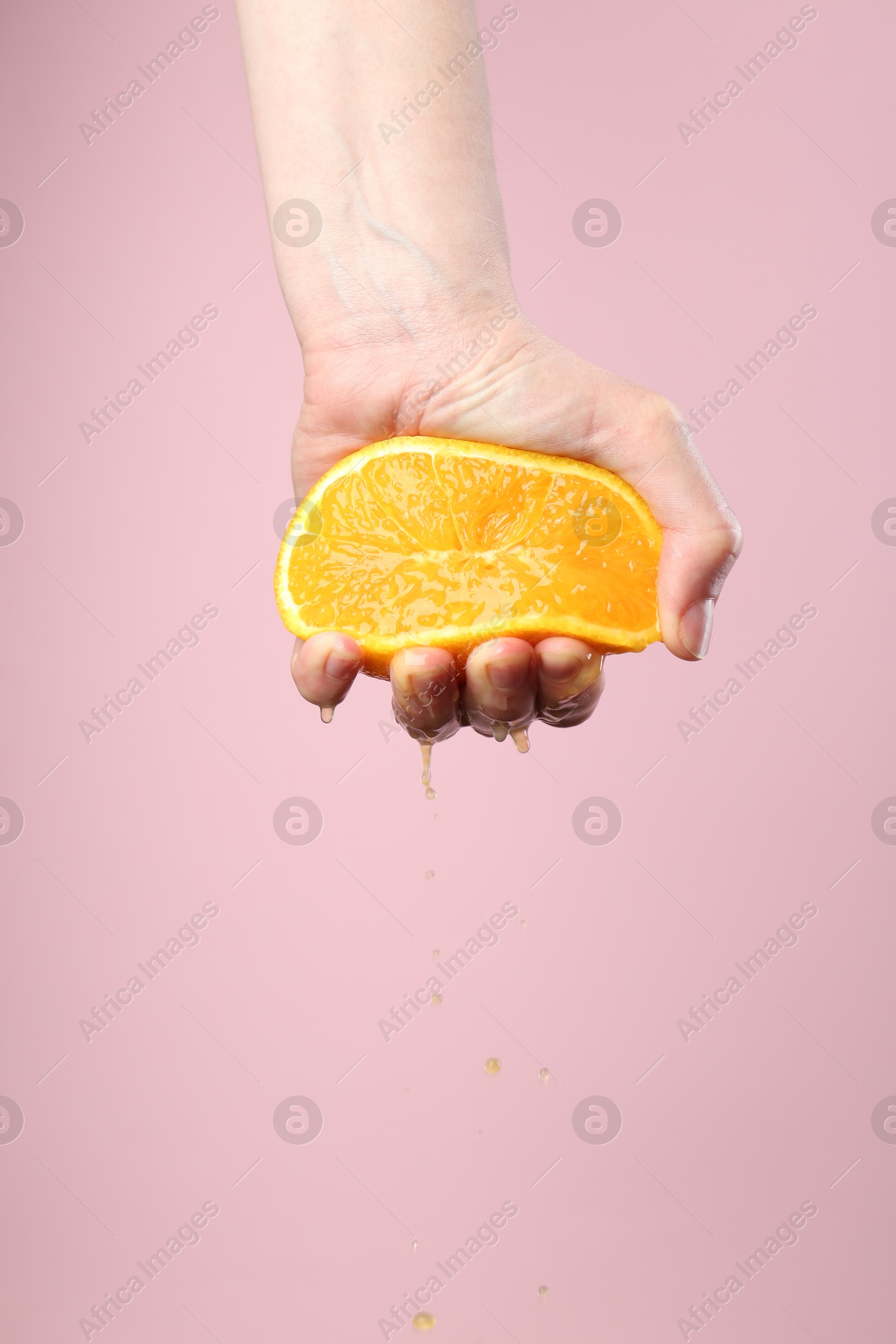 Woman squeezing orange on pink background, closeup. Space for text Photo of Woman squeezing orange on pink background, closeup. Space for text