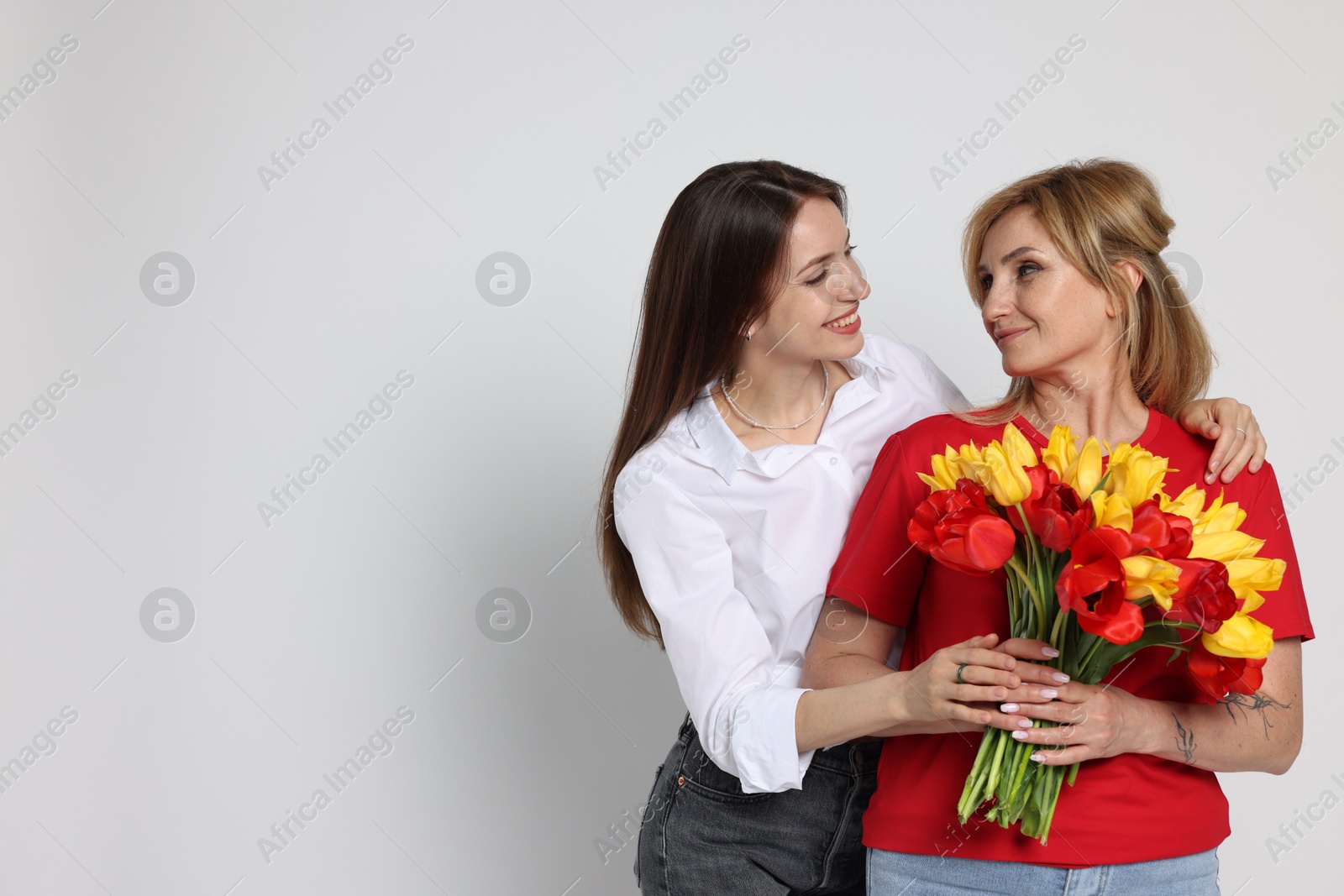 Woman giving her mother flowers on white background Photo of Woman giving her mother flowers on white background