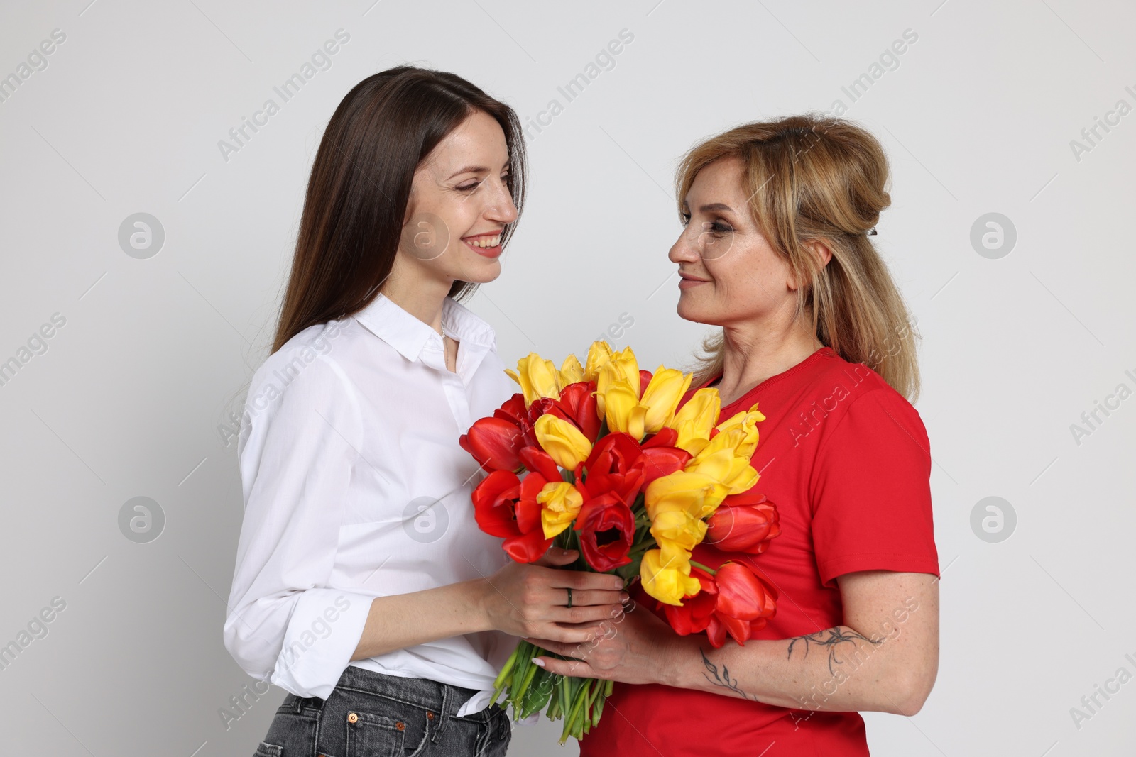 Woman giving her mother flowers on white background Photo of Woman giving her mother flowers on white background