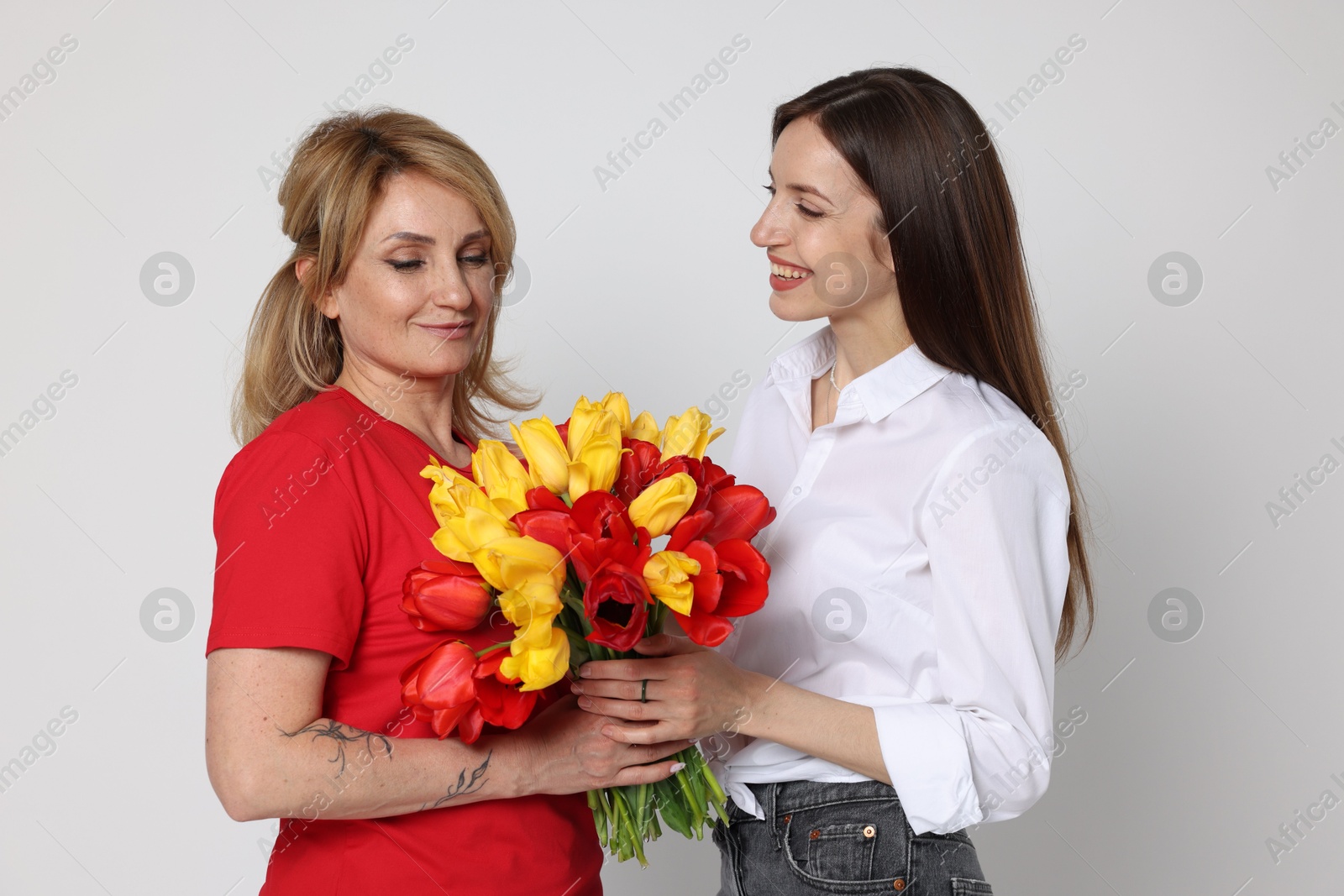 Woman giving her mother flowers on white background Photo of Woman giving her mother flowers on white background