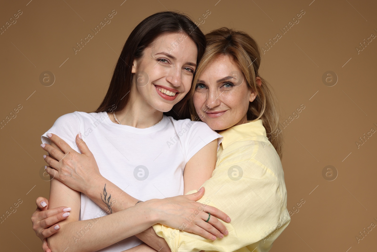 Mother and daughter hugging on light brown background Photo of Mother and daughter hugging on light brown background