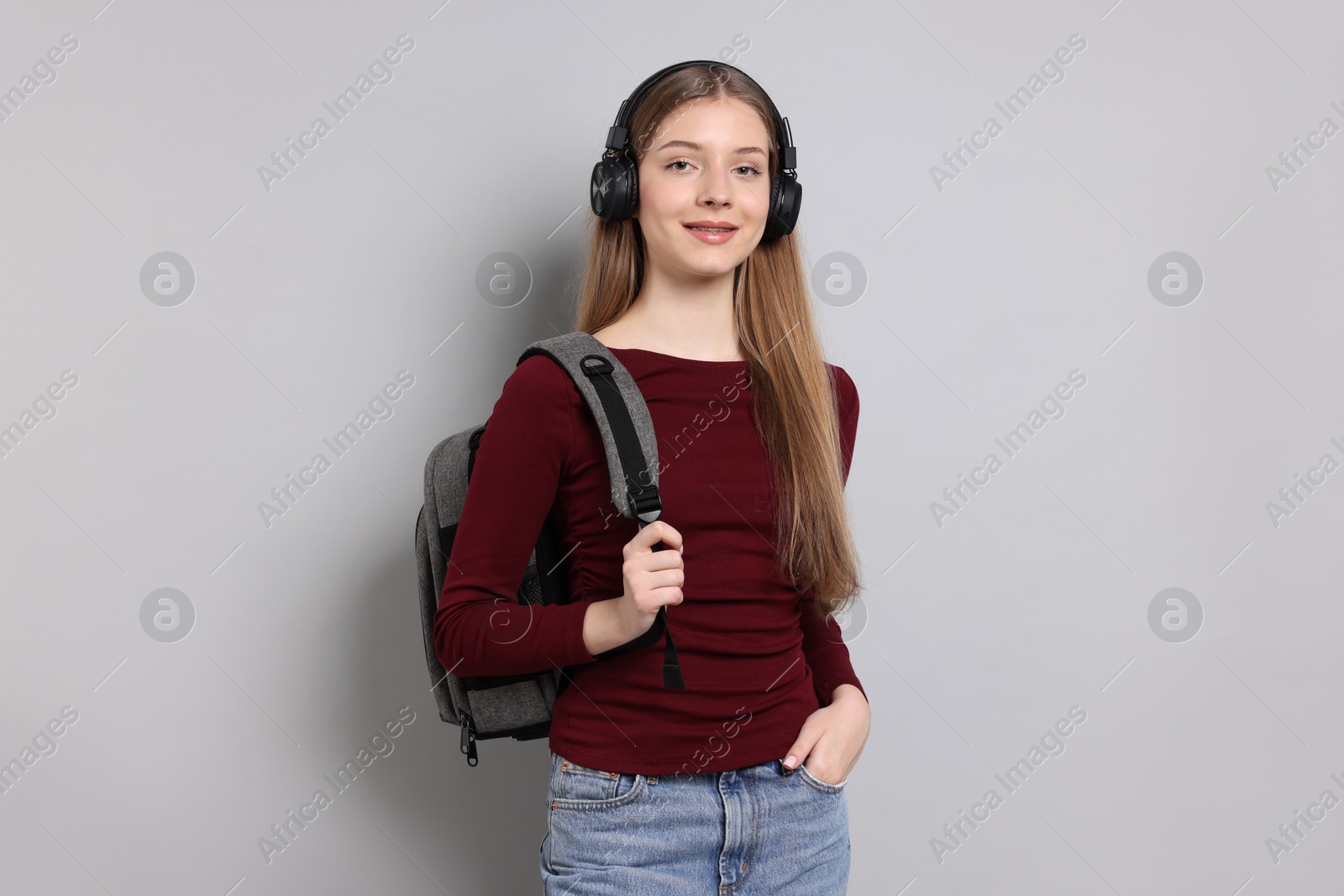 Photo of Teenage girl with headphones and backpack on light grey background