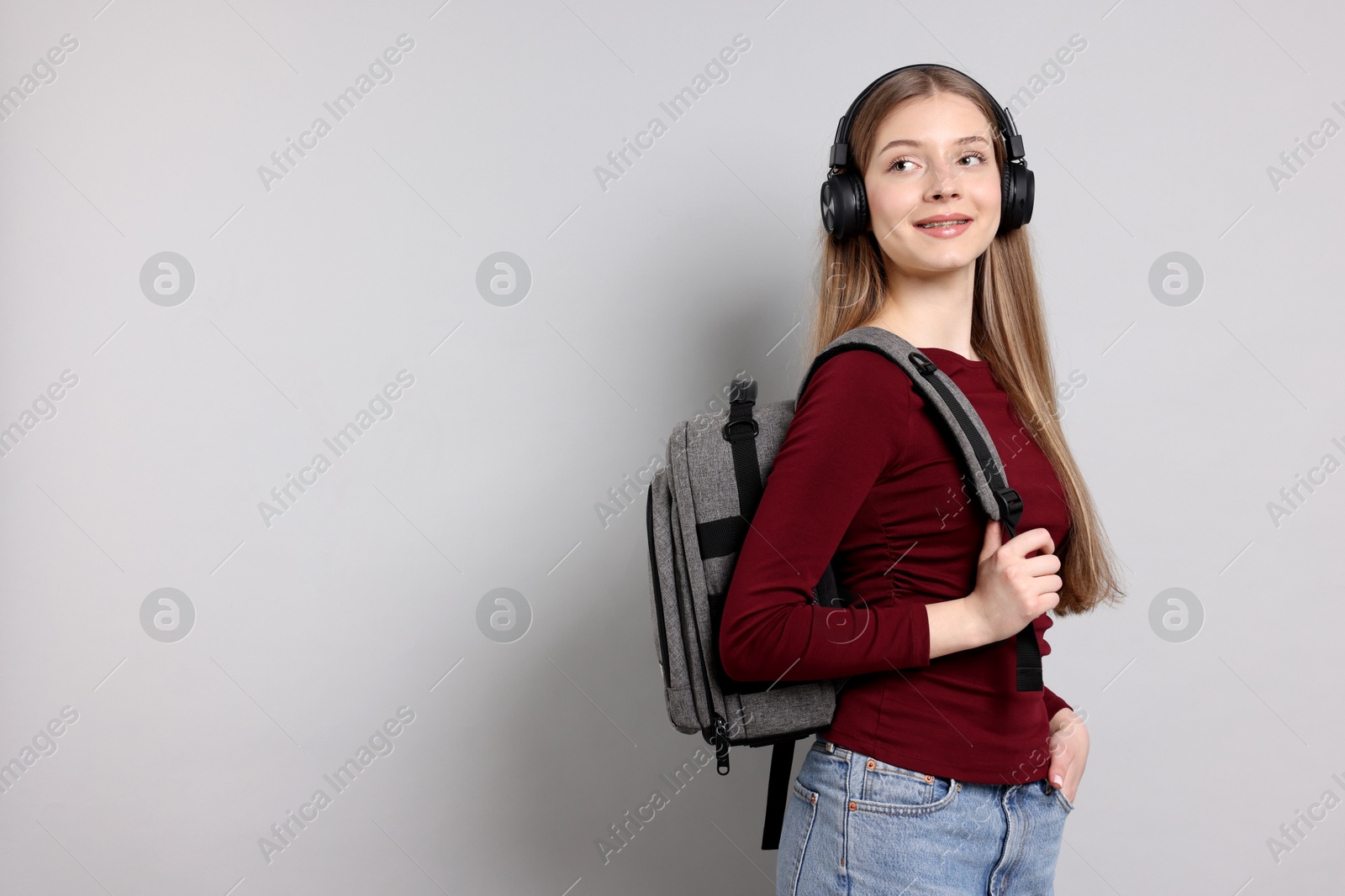 Photo of Teenage girl with headphones and backpack on light grey background. Space for text