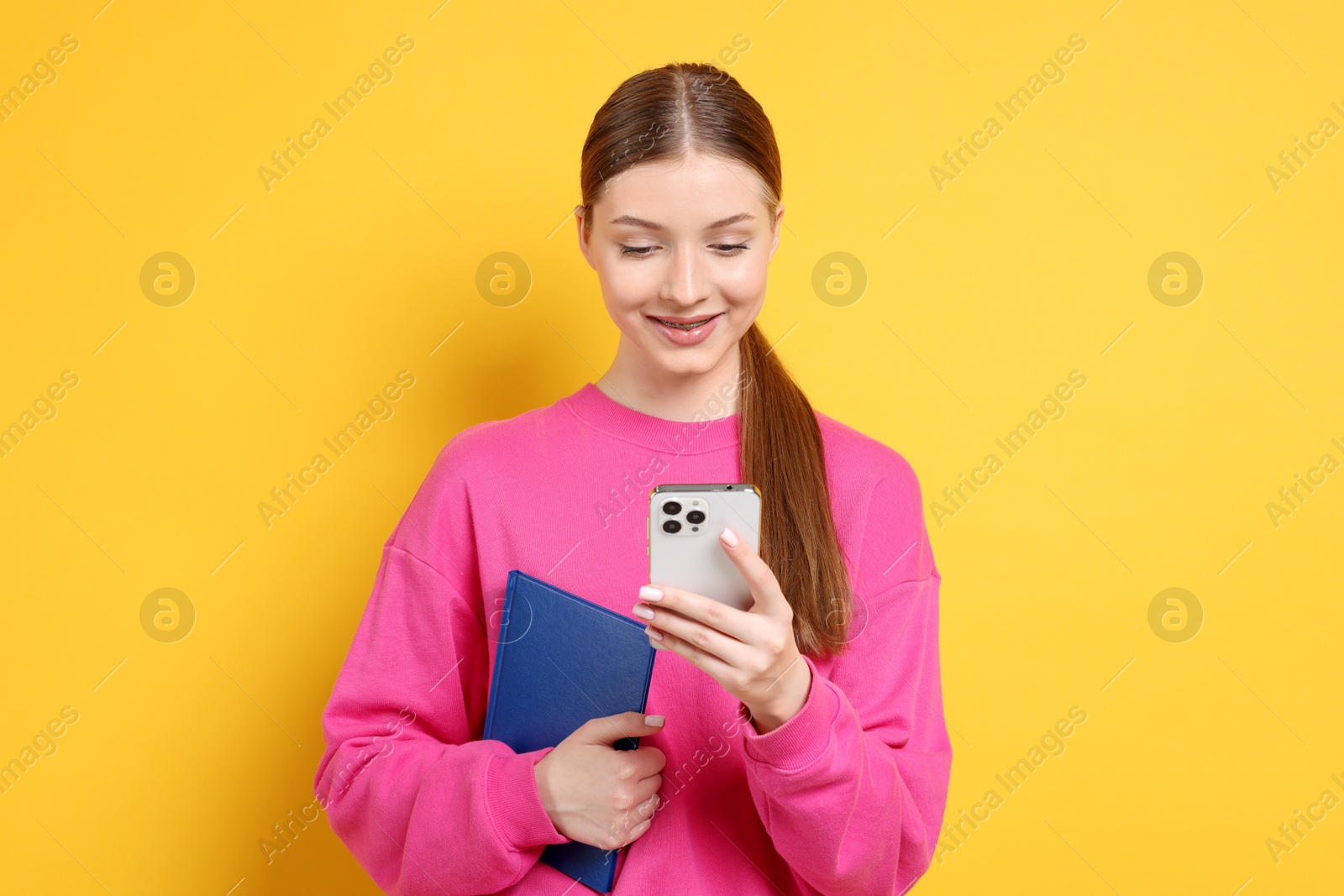 Photo of Teenage girl with smartphone and book on yellow background