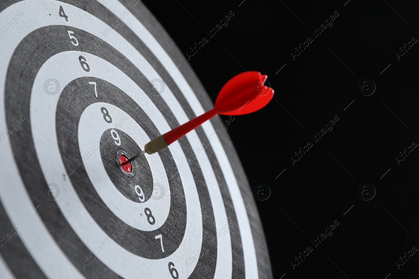 Targeting. Dart board with arrow on black background, closeup Photo of Targeting. Dart board with arrow on black background, closeup