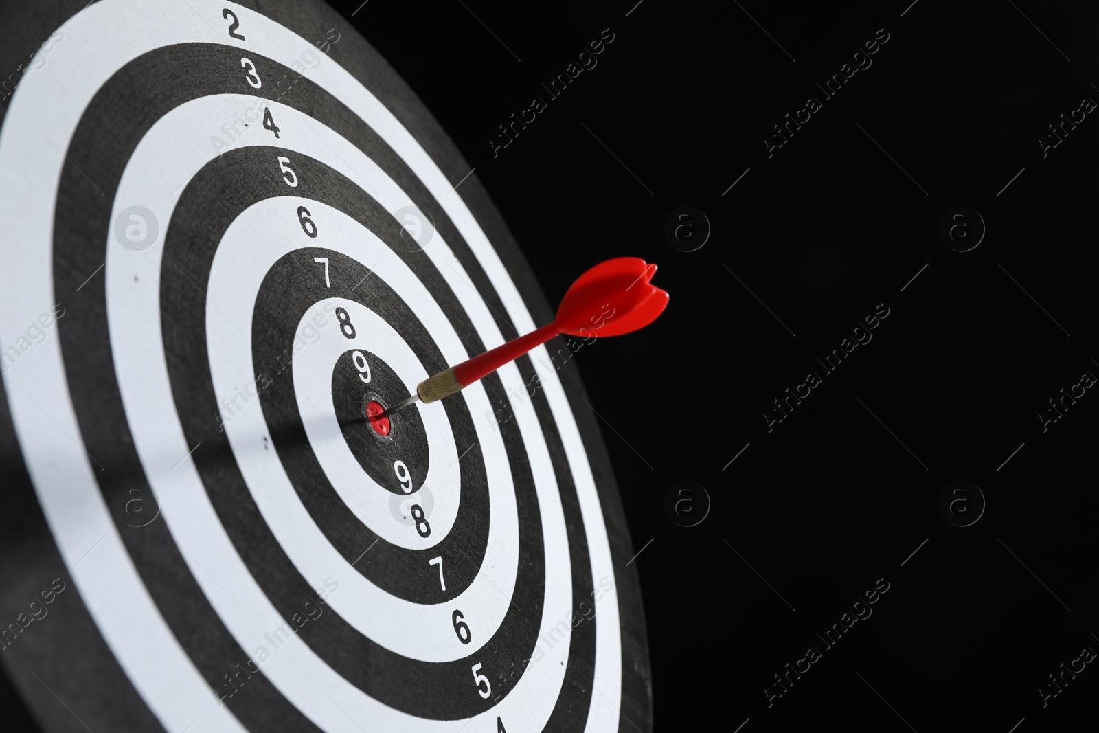 Targeting. Dart board with arrow on black background, closeup. Space for text Photo of Targeting. Dart board with arrow on black background, closeup. Space for text