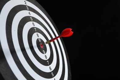 Photo of Targeting. Dart board with arrow on black background, closeup. Space for text