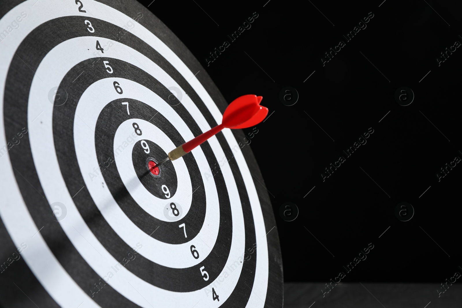 Targeting. Dart board with arrow on black background, closeup. Space for text Photo of Targeting. Dart board with arrow on black background, closeup. Space for text