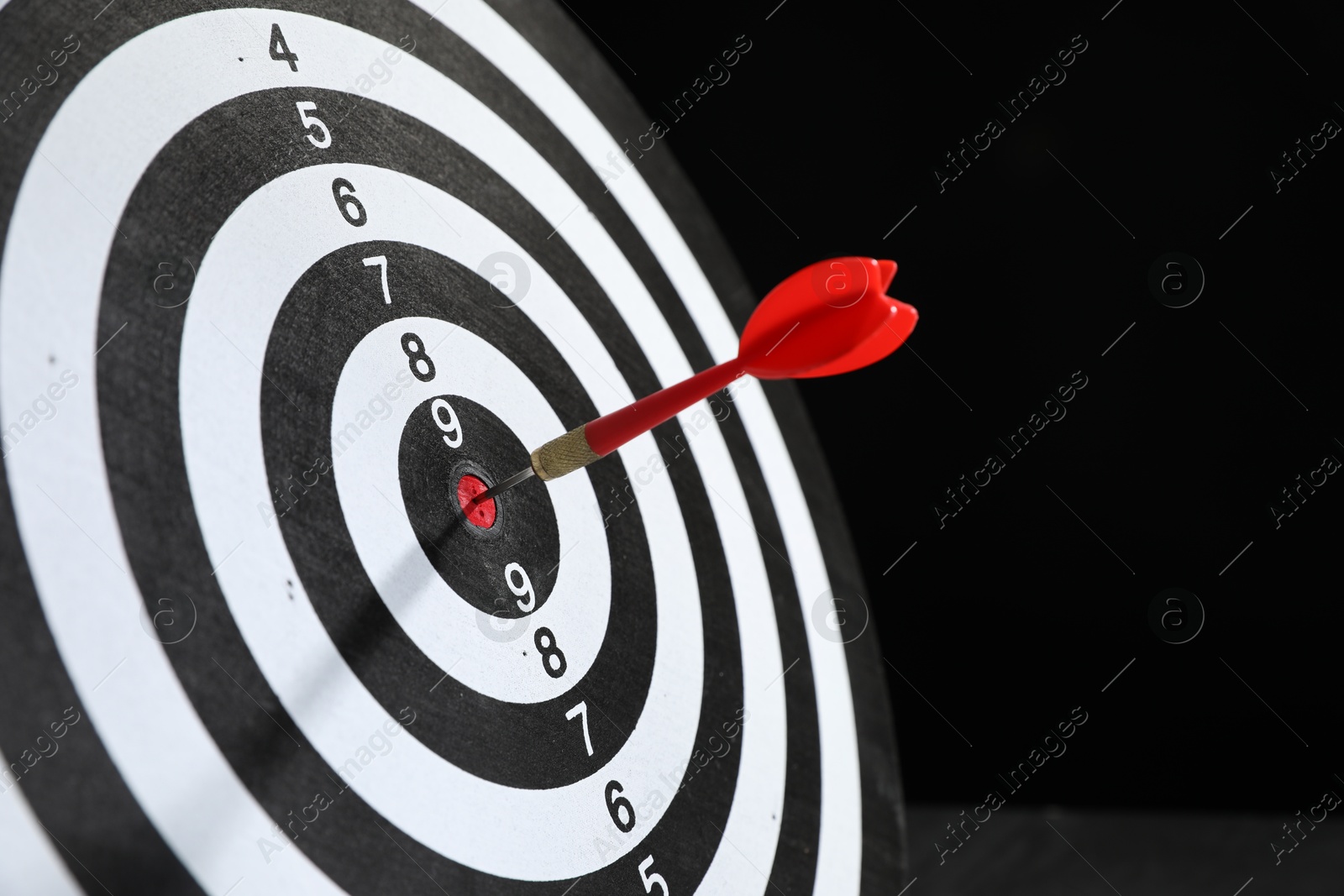 Targeting. Dart board with arrow on black background, closeup Photo of Targeting. Dart board with arrow on black background, closeup