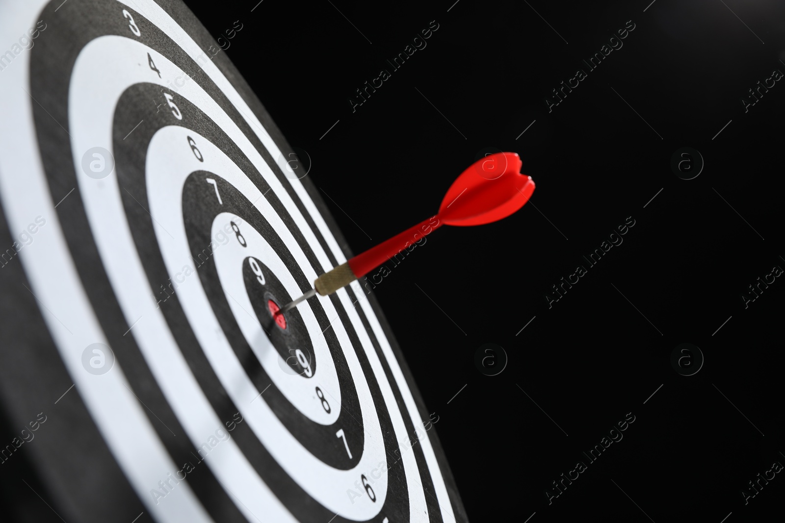 Targeting. Dart board with arrow on black background, closeup Photo of Targeting. Dart board with arrow on black background, closeup