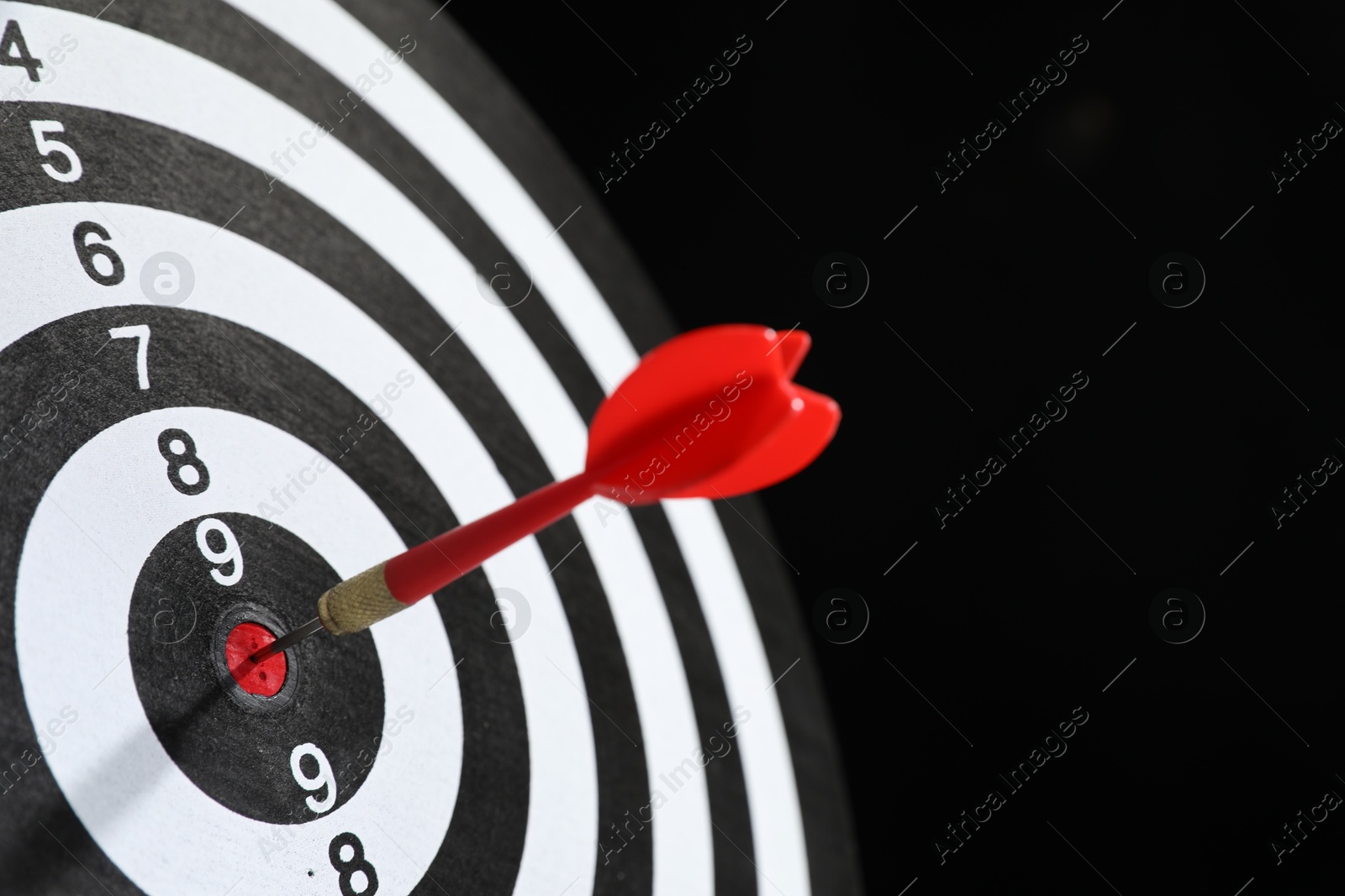 Targeting. Dart board with arrow on black background, closeup. Space for text Photo of Targeting. Dart board with arrow on black background, closeup. Space for text