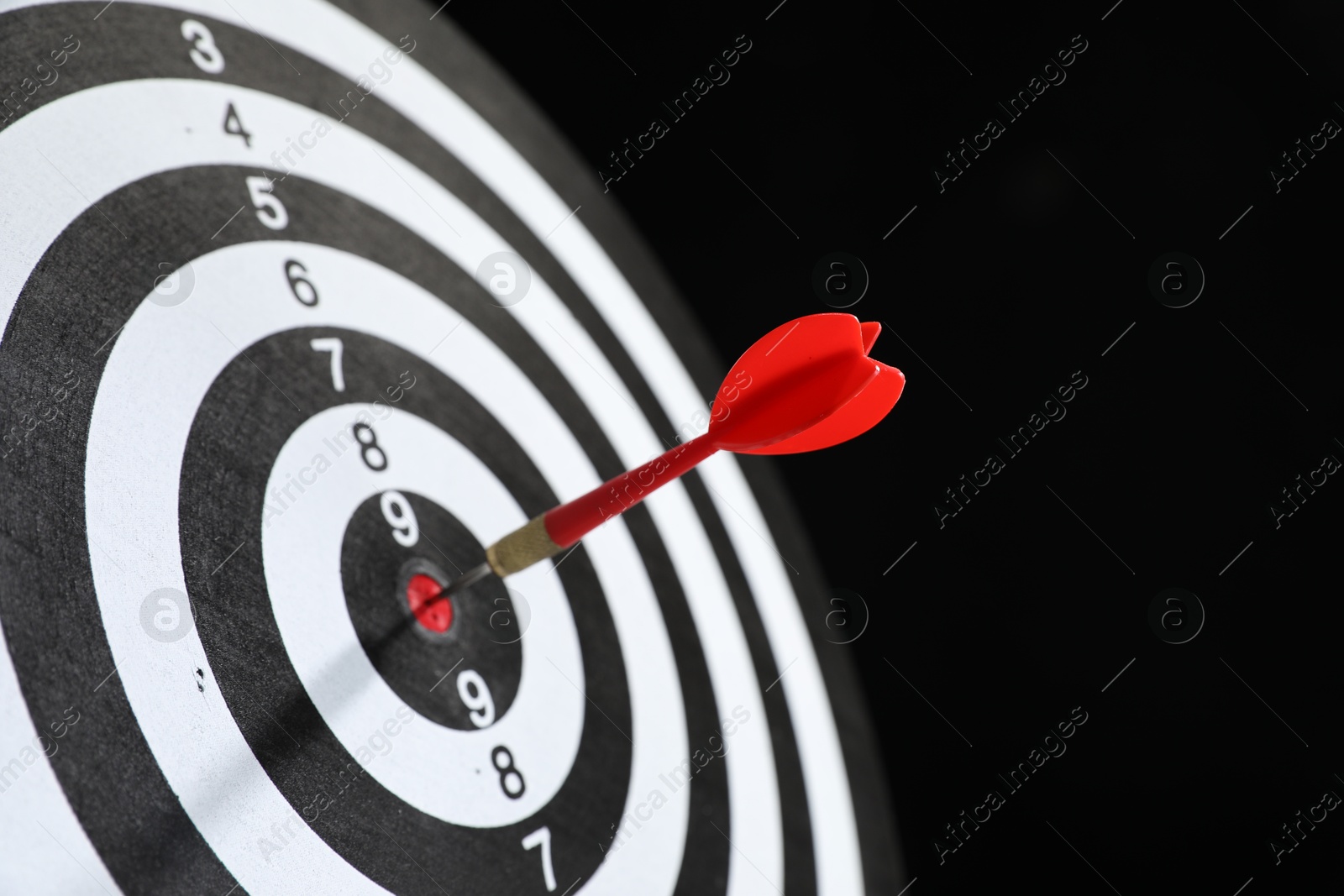 Targeting. Dart board with arrow on black background, closeup Photo of Targeting. Dart board with arrow on black background, closeup