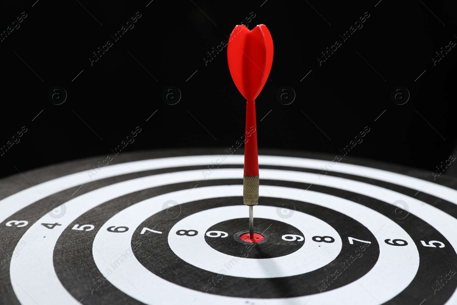 Targeting. Dart board with arrow on black background, closeup Photo of Targeting. Dart board with arrow on black background, closeup