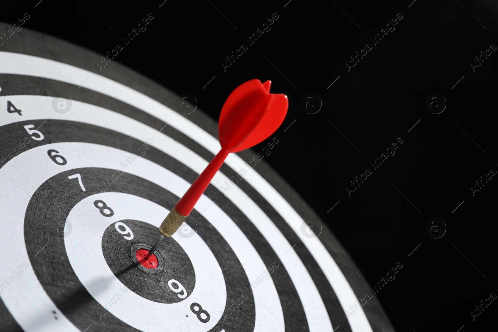 Targeting. Dart board with arrow on black background, closeup Photo of Targeting. Dart board with arrow on black background, closeup