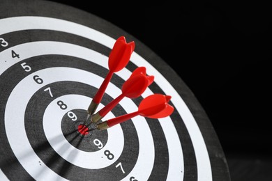 Photo of Targeting. Dart board with arrows on black background, closeup