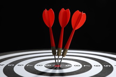 Photo of Targeting. Dart board with arrows on black background, closeup