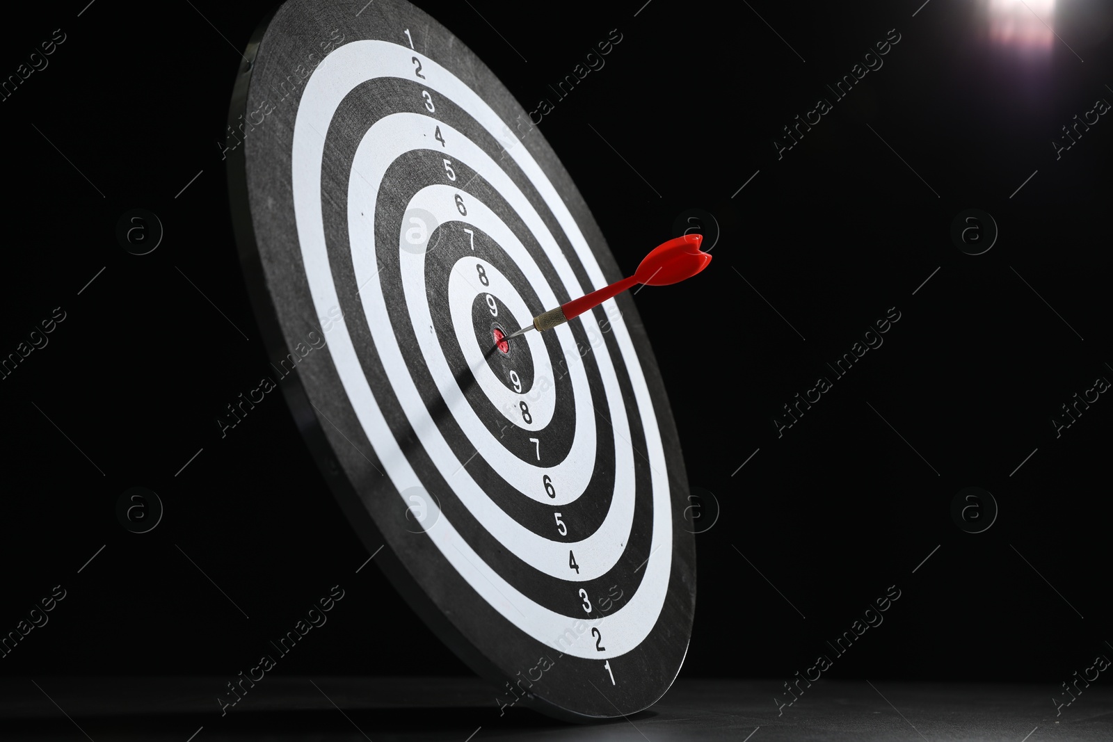 Targeting. Dart board with arrow on gray surface against black background Photo of Targeting. Dart board with arrow on gray surface against black background