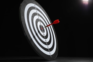 Photo of Targeting. Dart board with arrow on gray surface against black background