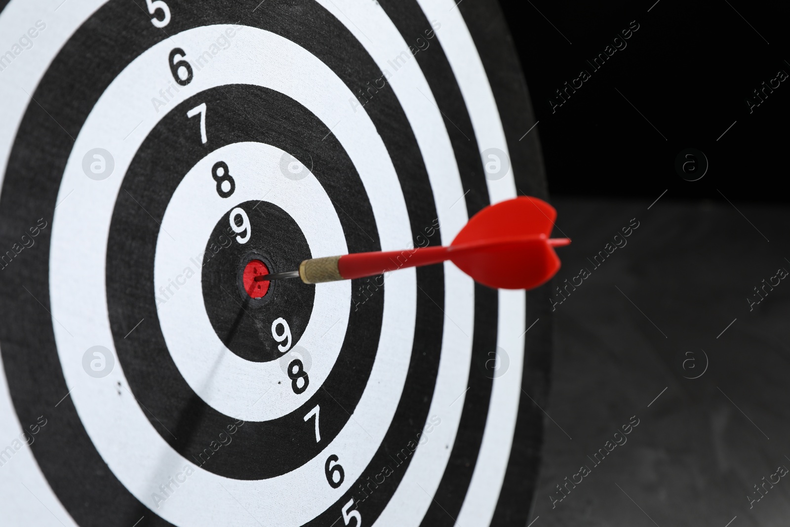 Targeting. Dart board with arrow on dark background, closeup Photo of Targeting. Dart board with arrow on dark background, closeup