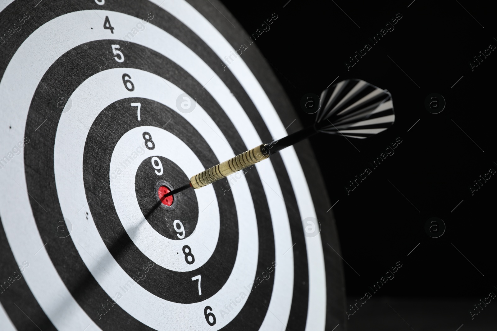 Targeting. Dart board with arrow on dark background, closeup Photo of Targeting. Dart board with arrow on dark background, closeup