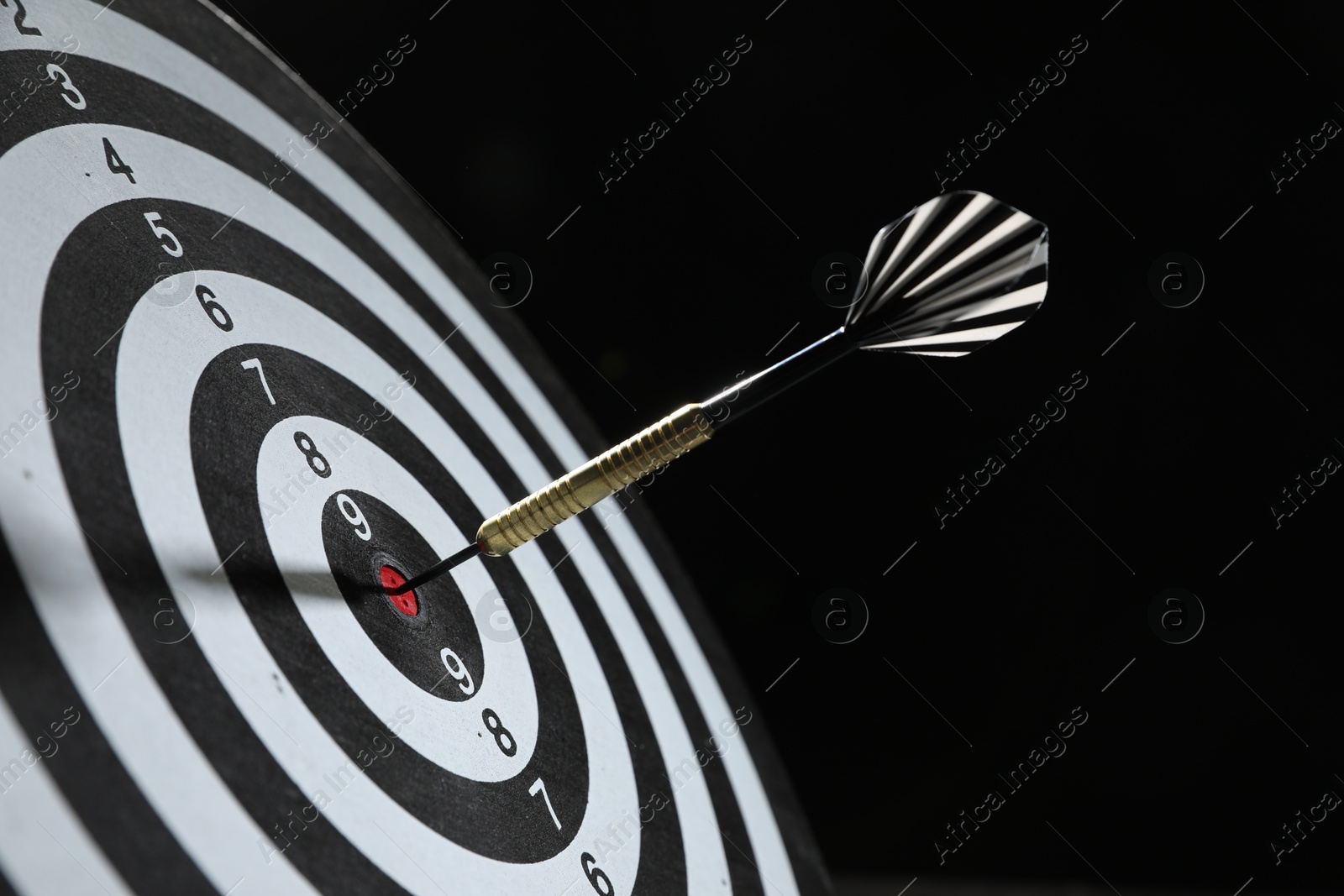 Targeting. Dart board with arrow on black background, closeup Photo of Targeting. Dart board with arrow on black background, closeup