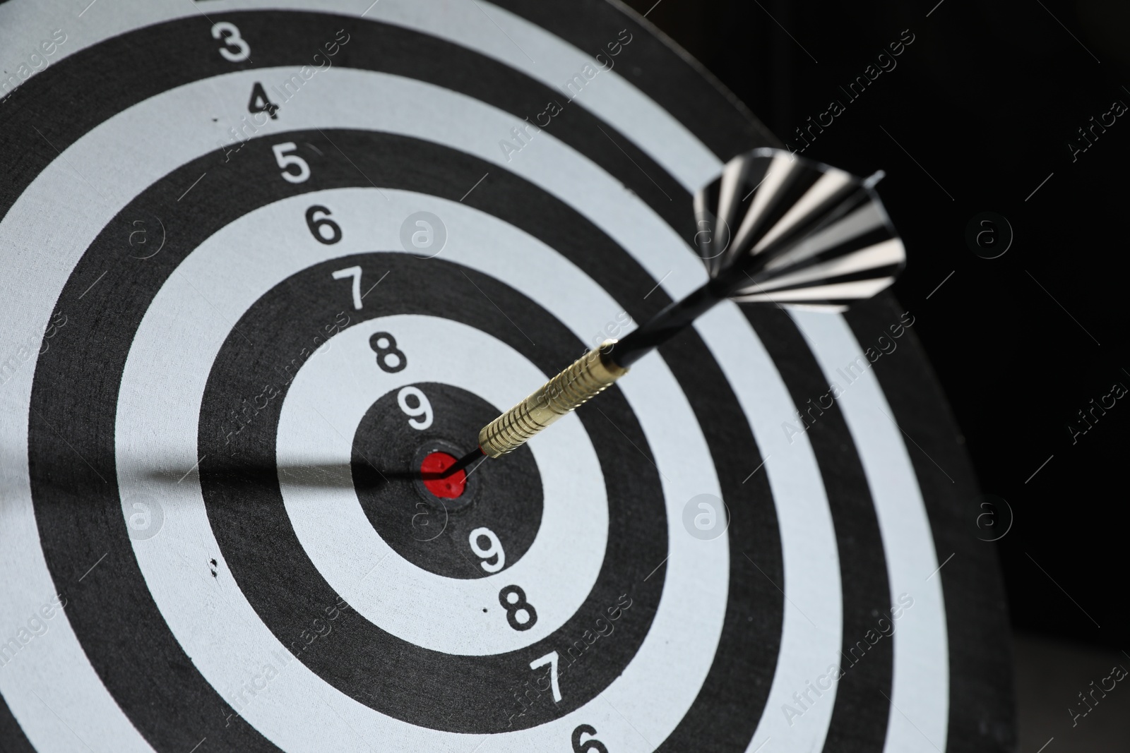 Targeting. Dart board with arrow on black background, closeup Photo of Targeting. Dart board with arrow on black background, closeup
