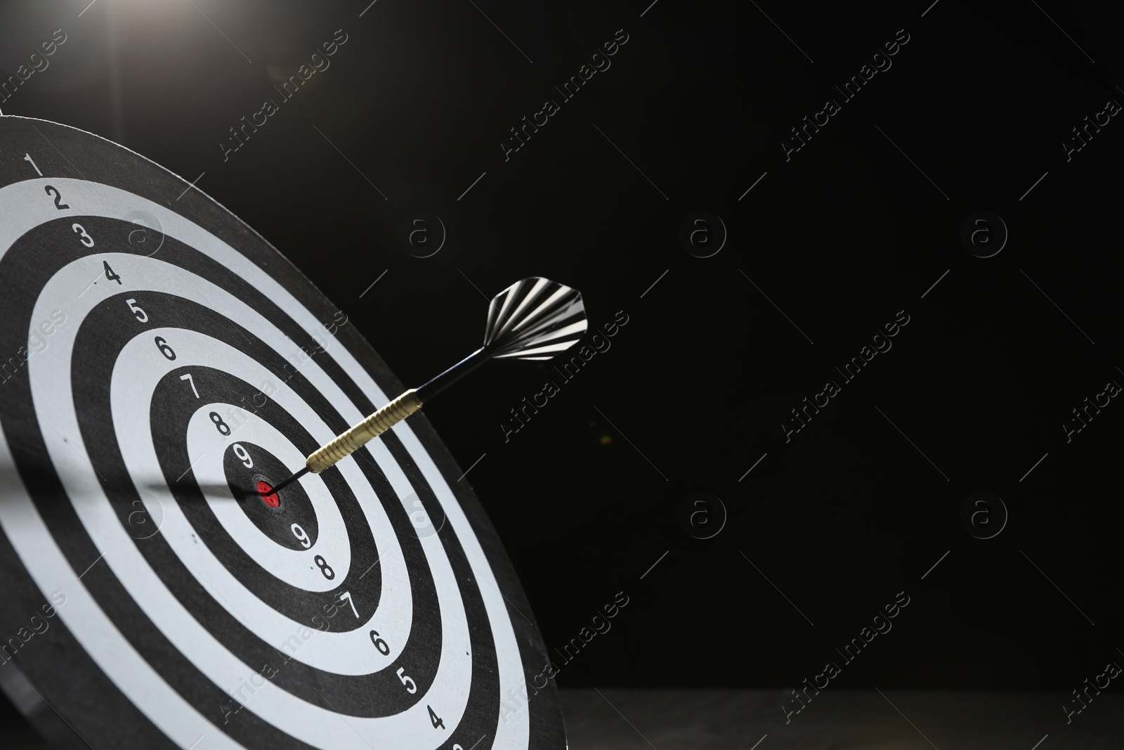 Targeting. Dart board with arrow on dark background, space for text Photo of Targeting. Dart board with arrow on dark background, space for text
