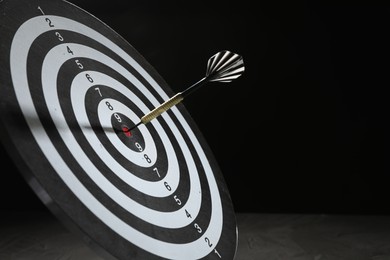 Photo of Targeting. Dart board with arrow on dark background, closeup. Space for text